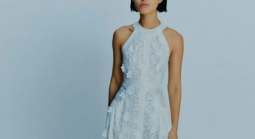 Ein Model trägt ein weißes Spitzenkleid mit Blumenapplikationen. Welche Farbe passt zu Himmelblau? Dieses Kleid ist eine zarte Antwort.