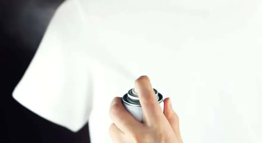 Hand sprüht mit einer Dose auf ein weißes T-Shirt, um statische Aufladung zu verhindern.