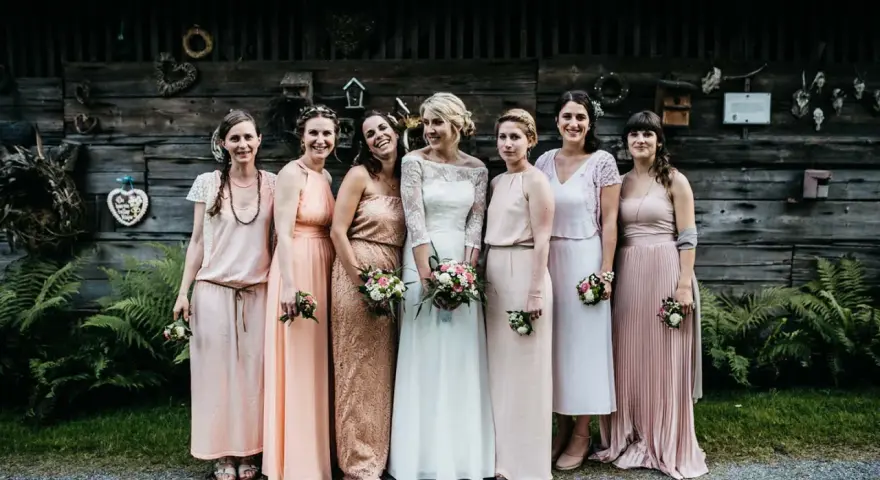 Brautjungfern in zarten Pastelltönen posieren vor rustikaler Holzwand, ein Bild von einer entspannten boho hochzeit.
