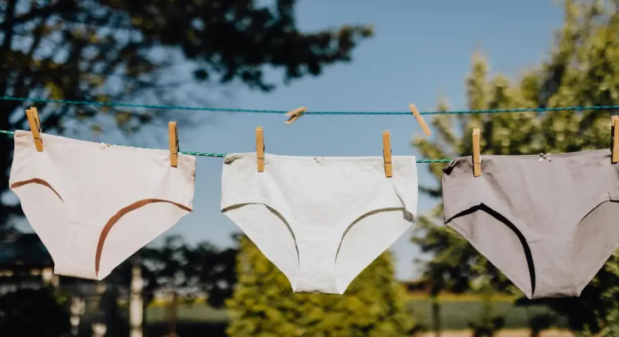 Drei Unterhosen in verschiedenen Grautönen trocknen an einer Wäscheleine. Das Bild zeigt den Prozess des Unterhosen waschen.