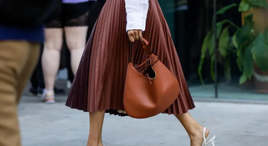 Elegant brauner Faltenrock, kombiniert mit weißer Bluse und cognacfarbener Tasche. Ein stilvoller Look für den Sommer.