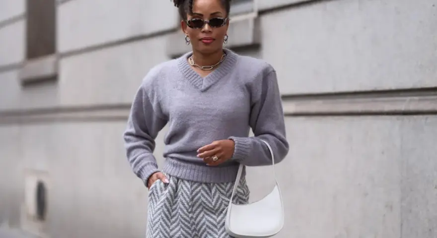 Eine Frau in grauem Pullover und Hose mit Zickzackmuster. Sie trägt eine weiße Tasche. Ein Beispiel, welche Farben passen zu grau.