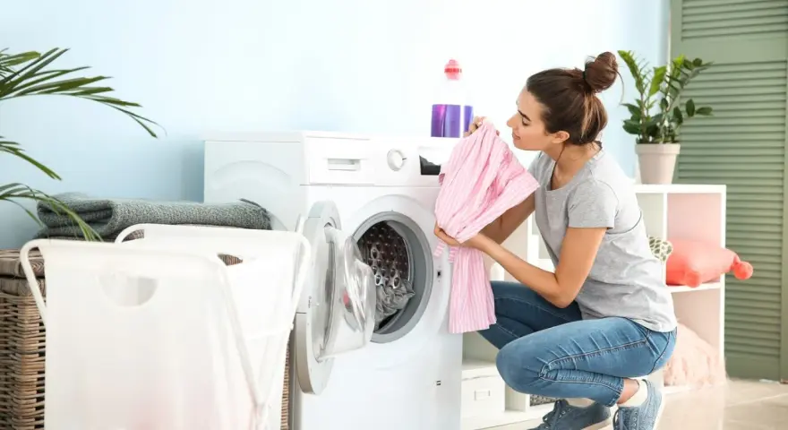 Junge Frau lädt Wäsche in die Waschmaschine. Sie hält ein rosa gestreiftes Kleidungsstück, bereit zum leinen waschen.