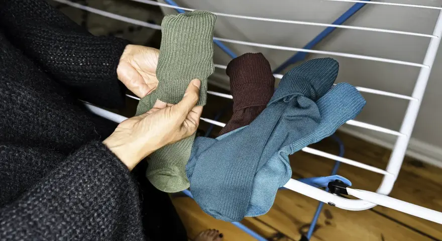 Hände sortieren frisch gewaschene, bunte Socken auf einem Wäscheständer.