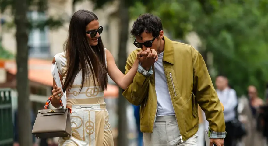 Ein Mann küsst die Hand einer Frau. Ihr **outfit erstes date** ist elegant: Sie trägt ein gemustertes Kleid, er eine olivgrüne Jacke.