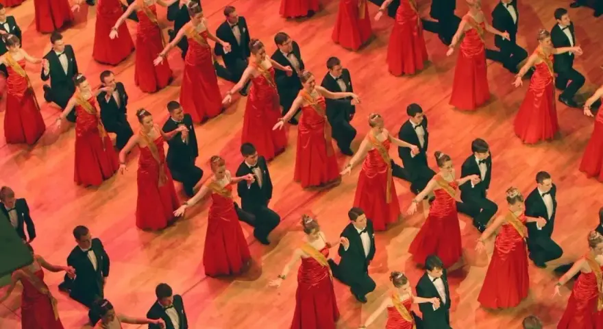 Junge Paare in roten Kleidern und schwarzen Anzügen tanzen. Die Kleiderordnung der Semperoper wird hier elegant umgesetzt.