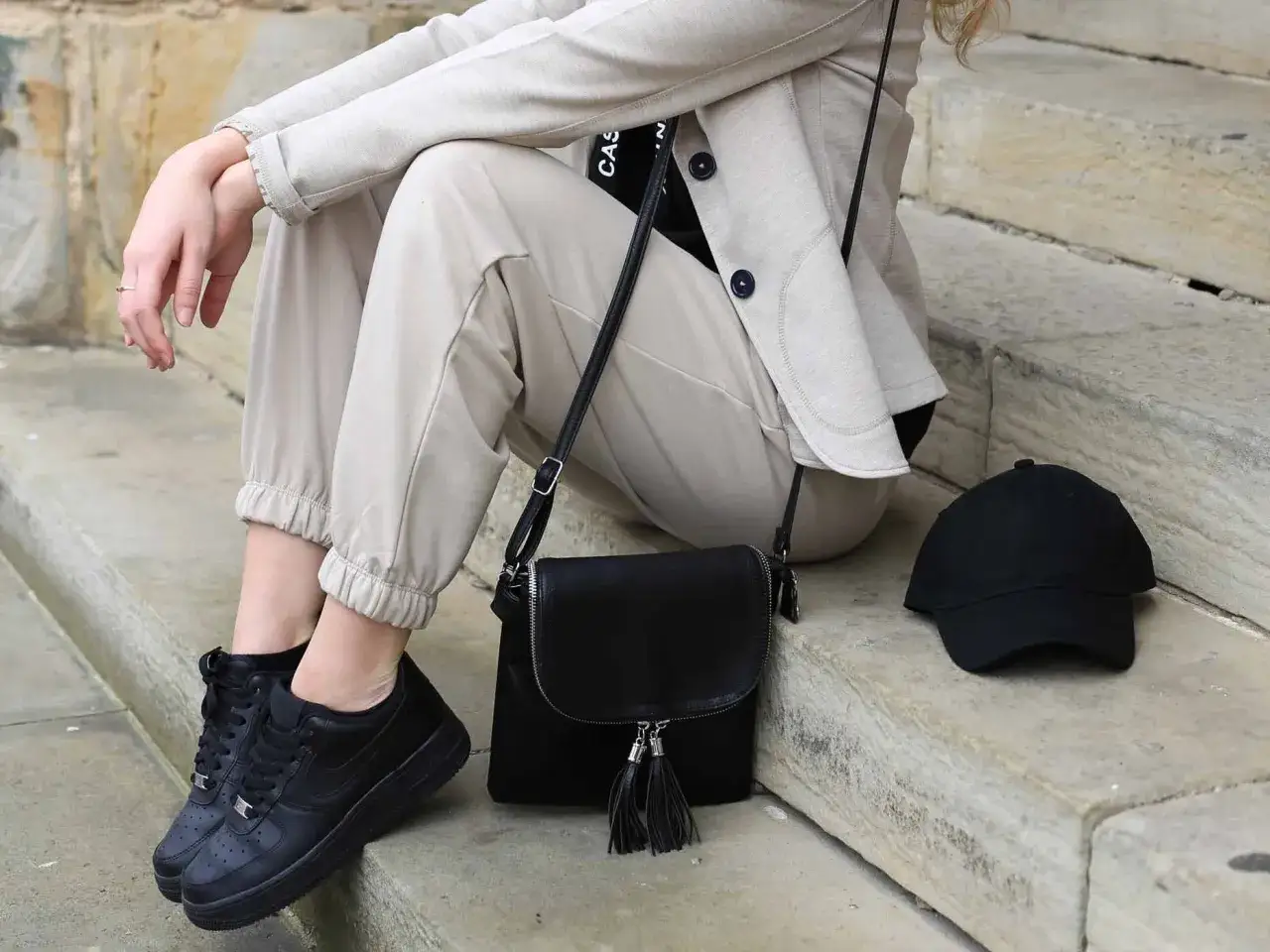 Stylisches flugzeug outfit damen: beige Blazer, Hose, schwarze Sneaker, Tasche und Cap. Perfekt für die Reise.