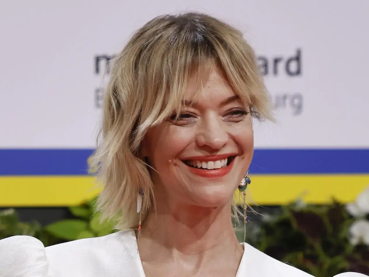 Lachende Frau mit stufig fransig bob frisuren gestuft ab 50. Ihr blondes Haar fällt locker um ihr Gesicht.