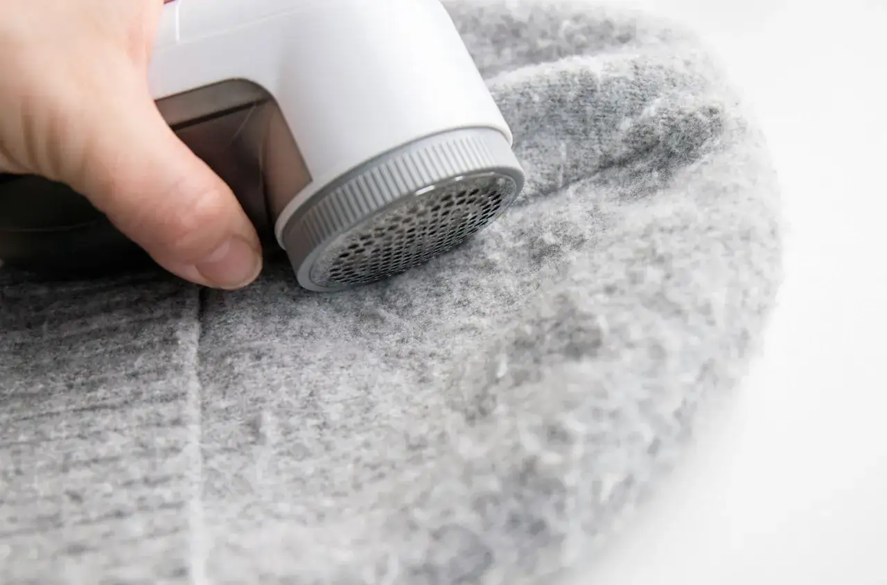 Ein Wollpullover, der eingelaufen ist, wird mit einem Fusselrasierer behandelt. Die Fasern werden entfernt, um das Kleidungsst&uuml;ck wieder glatt zu machen.