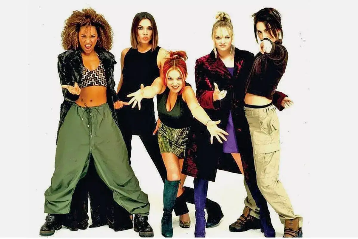 F&uuml;nf Frauen im 2000er Style posieren selbstbewusst. Ihre Outfits, von Baggy Pants bis zu kurzen R&ouml;cken, spiegeln den damaligen Zeitgeist wider.