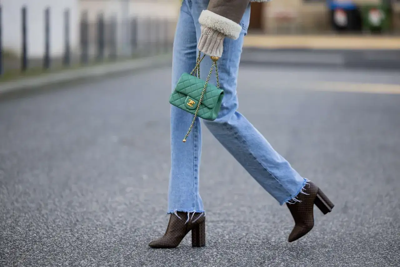 Modische Frau kombiniert lässige Jeans mit auffälligen Boots und einer grünen Chanel-Tasche.