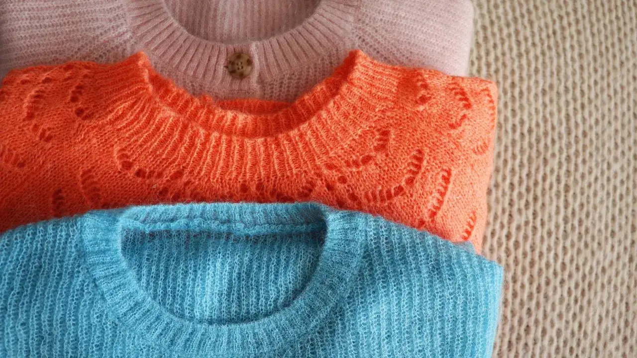 Drei gestapelte Pullover in Rosa, Orange und Blau. So kannst du deine Wolle richtig waschen und die Farben erhalten.