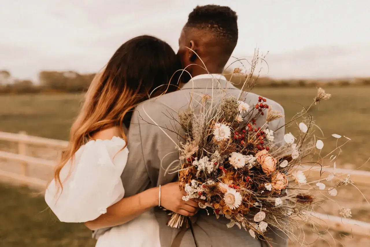 Brautpaar umarmt sich, sie hält einen wilden Blumenstrauß. Perfekt für eine boho hochzeit.