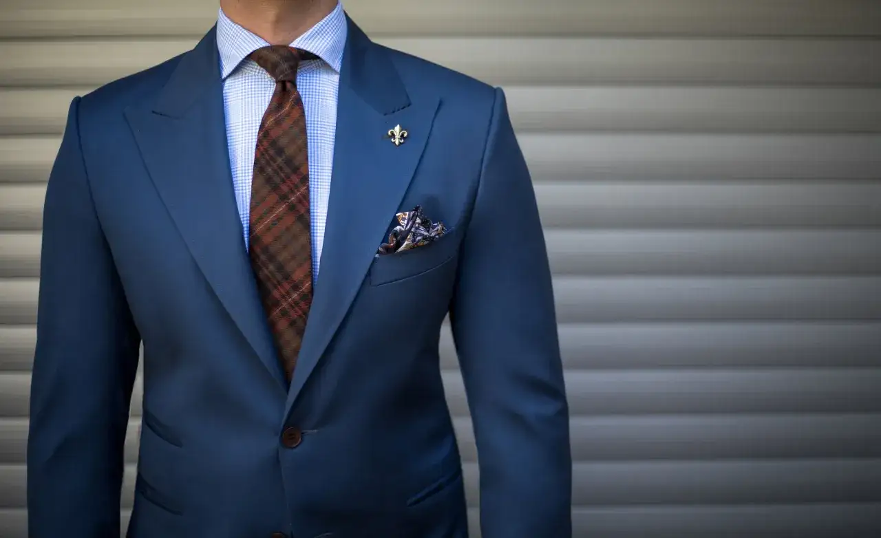 Eleganter blauer Anzug mit kariertem Hemd, brauner Krawatte und Einstecktuch.