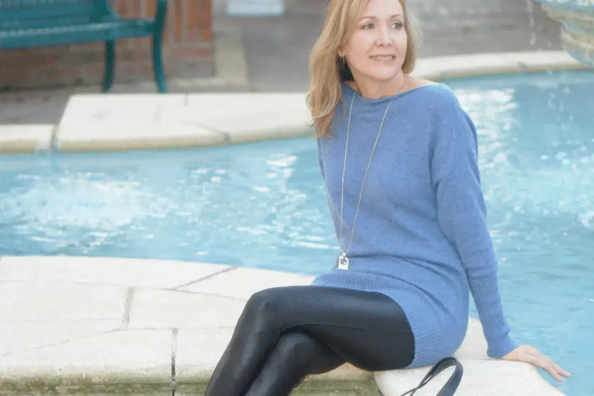 Frau sitzt am Poolrand, kombiniert eine blaue Tunika mit gl&auml;nzenden Leggings.
