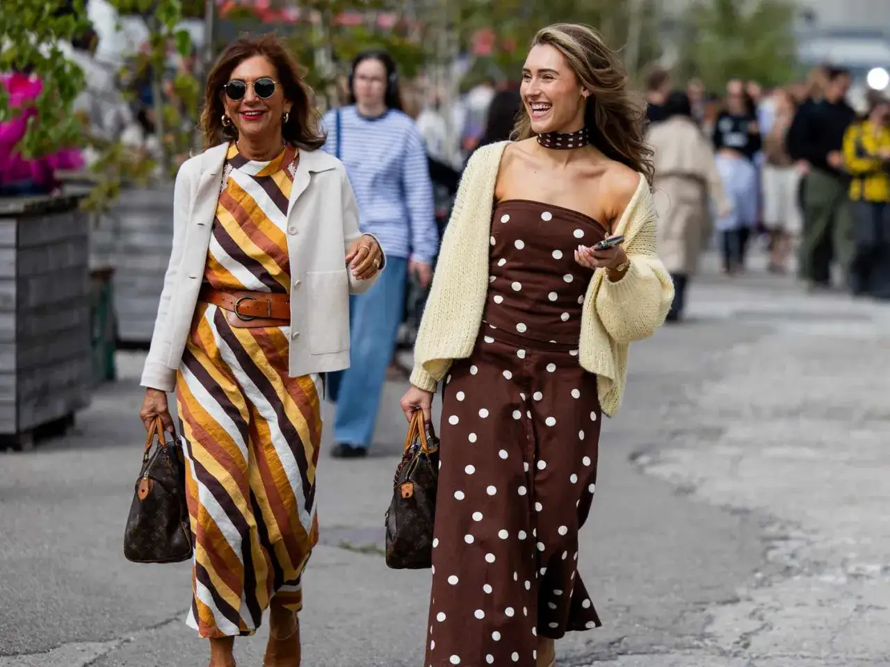 Zwei Frauen spazieren. Eine tr&auml;gt ein gestreiftes Kleid, die andere ein braunes Kleid mit Tupfen. Beide sind stilvoll gekleidet und zeigen, wie man ein braunes Kleid kombinieren kann.