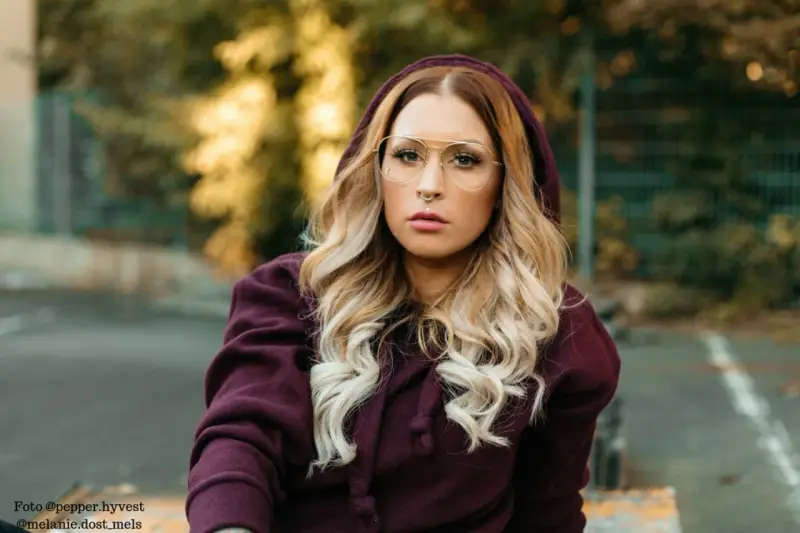 Frau mit blonden Haaren und Brille trägt einen Kapuzenpullover in dunklem Beere. Die Farbe Beere kombiniert sie gekonnt mit ihrem Outfit.