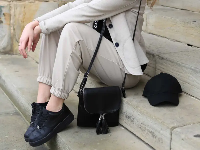 Stylisches flugzeug outfit damen: beige Hose, Blazer, schwarze Sneaker, Tasche und Cap. Perfekt für die Reise.