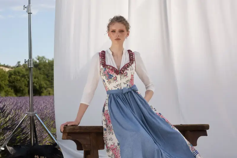 Ein Dirndl im floralen Muster mit blauem Rock, ein moderner Dirndl-Trend, posiert vor Lavendelfeld-Kulisse.